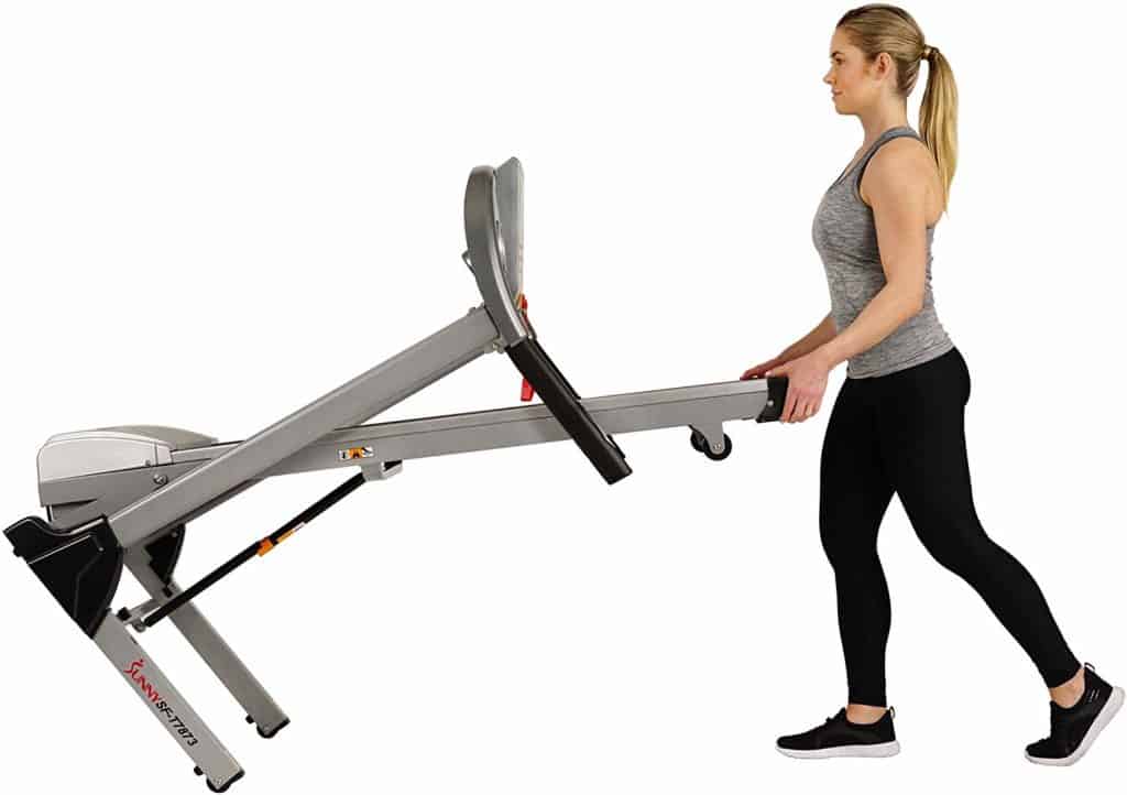 The Sunny Health & Fitness Electric Folding Treadmill SF-T7873 is being moved to storage by a lady