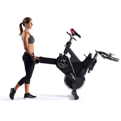 A lady is moving the SOLE SB900 Indoor Exercise Bike to storage