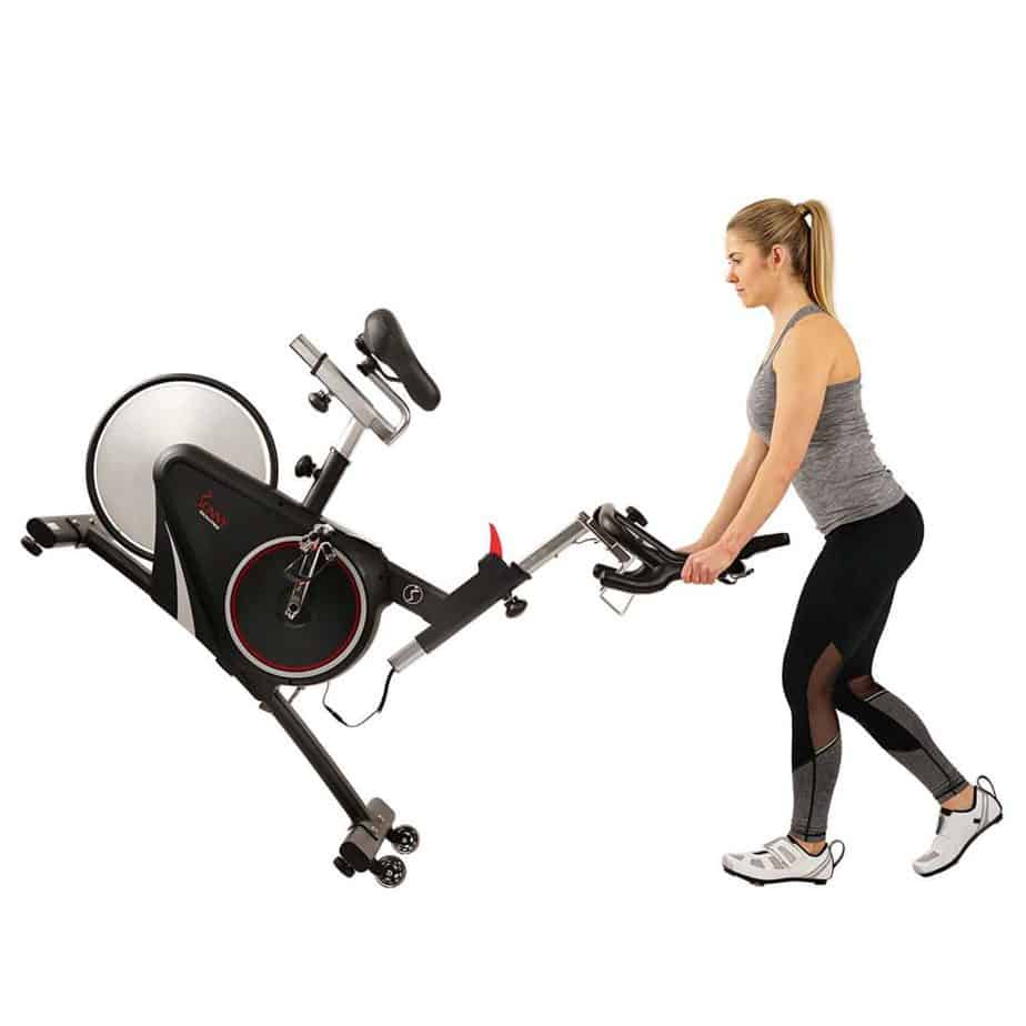 A lady rolling away the Sunny Health & Fitness SF-B1709 Indoor Cycling Bike to storage