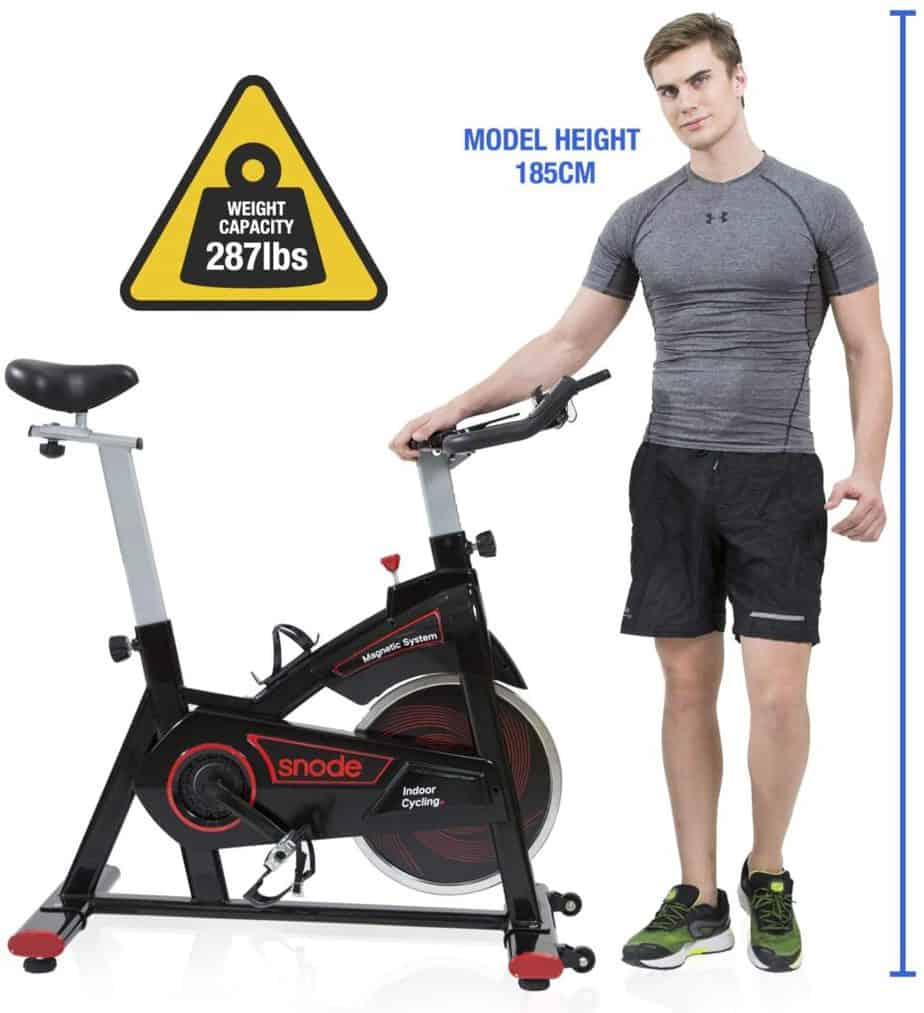 A 6' tall man standing by the SNODE 8731 Indoor Cycling Bike 