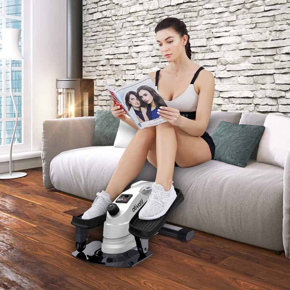 A lady works out with the Ativafit Under-Desk Elliptical Bike while sitting on a couch