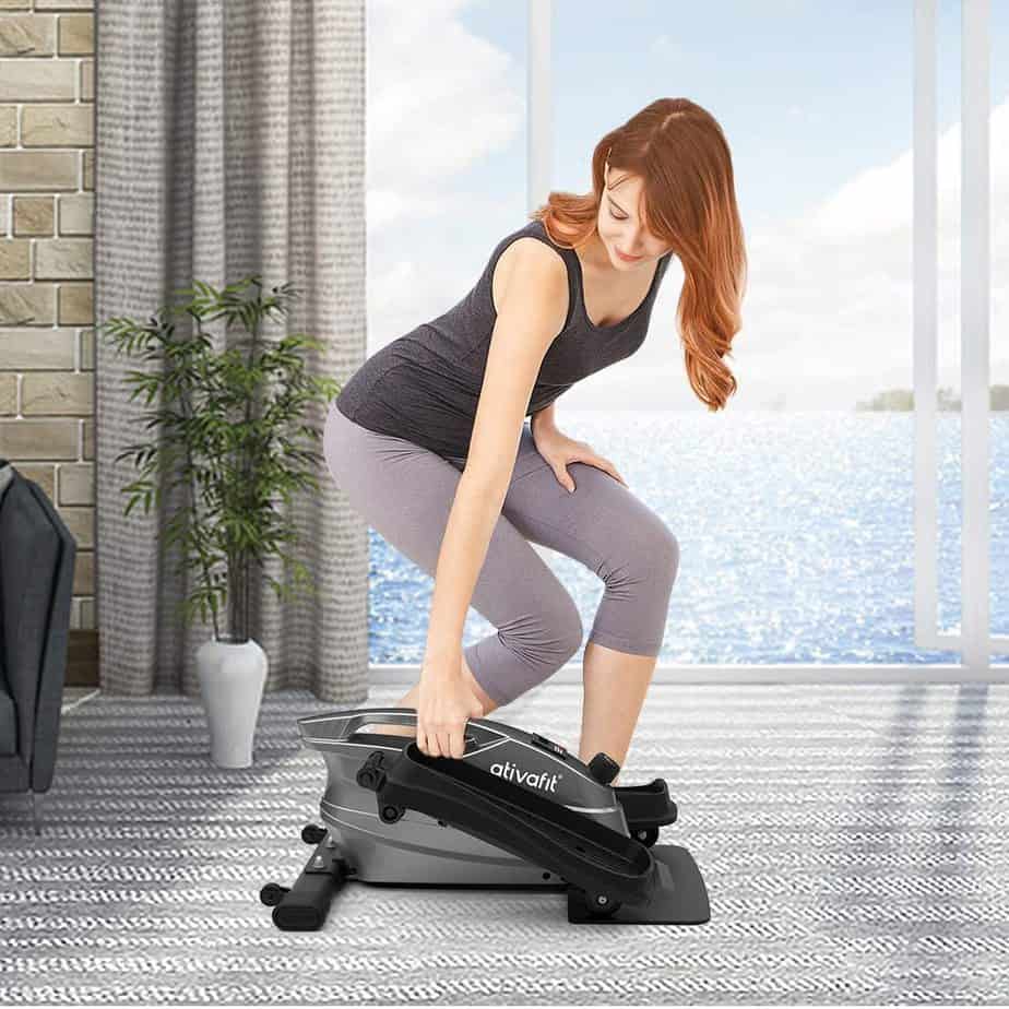 A lady lifts the Ativafit Under-Desk Elliptical Bike by the handle for storage