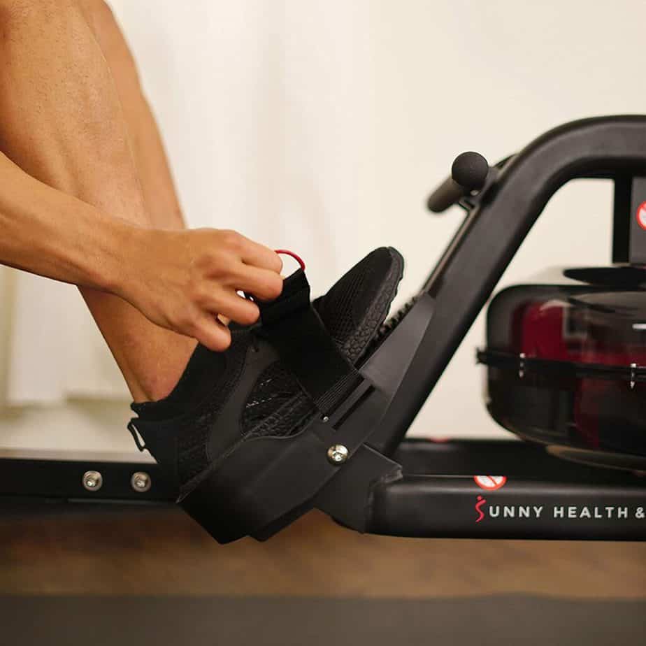 A man straps this foot on the pedal of the Sunny Health & Fitness SF-RW5713 Obsidian Surge 500 Rowing Machine 