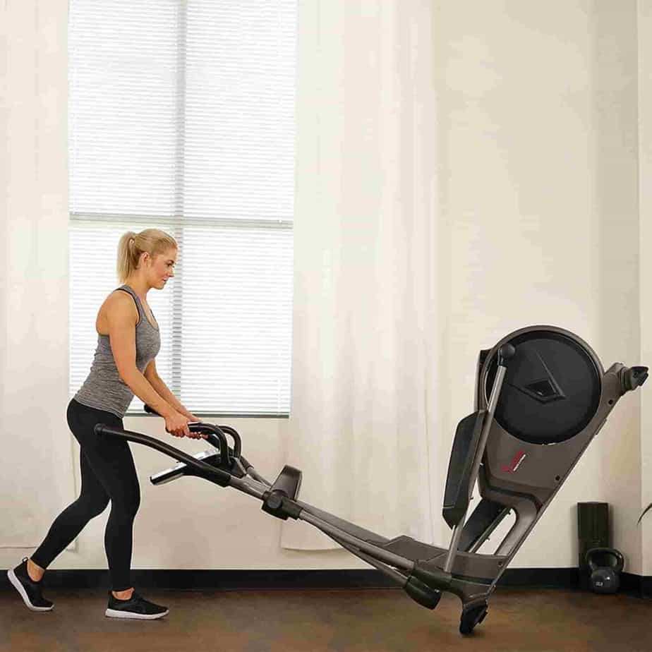 The lady rolls the Sunny SF-E3912 Magnetic Elliptical Trainer away for storage