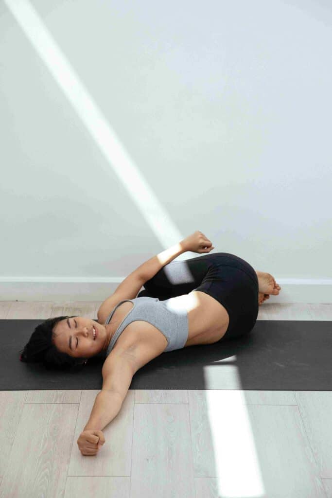 A lady does the spinal twist stretching on a yoga mat